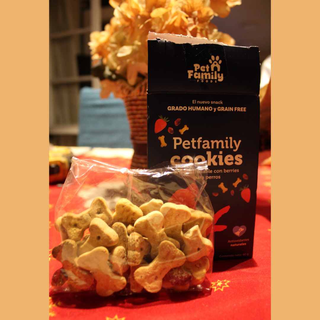 Fotografía real de las galletas PetFamily con forma de hueso dentro de una bolsa transparente, situada junto a su caja original para mostrar el tamaño y la textura real del snack.