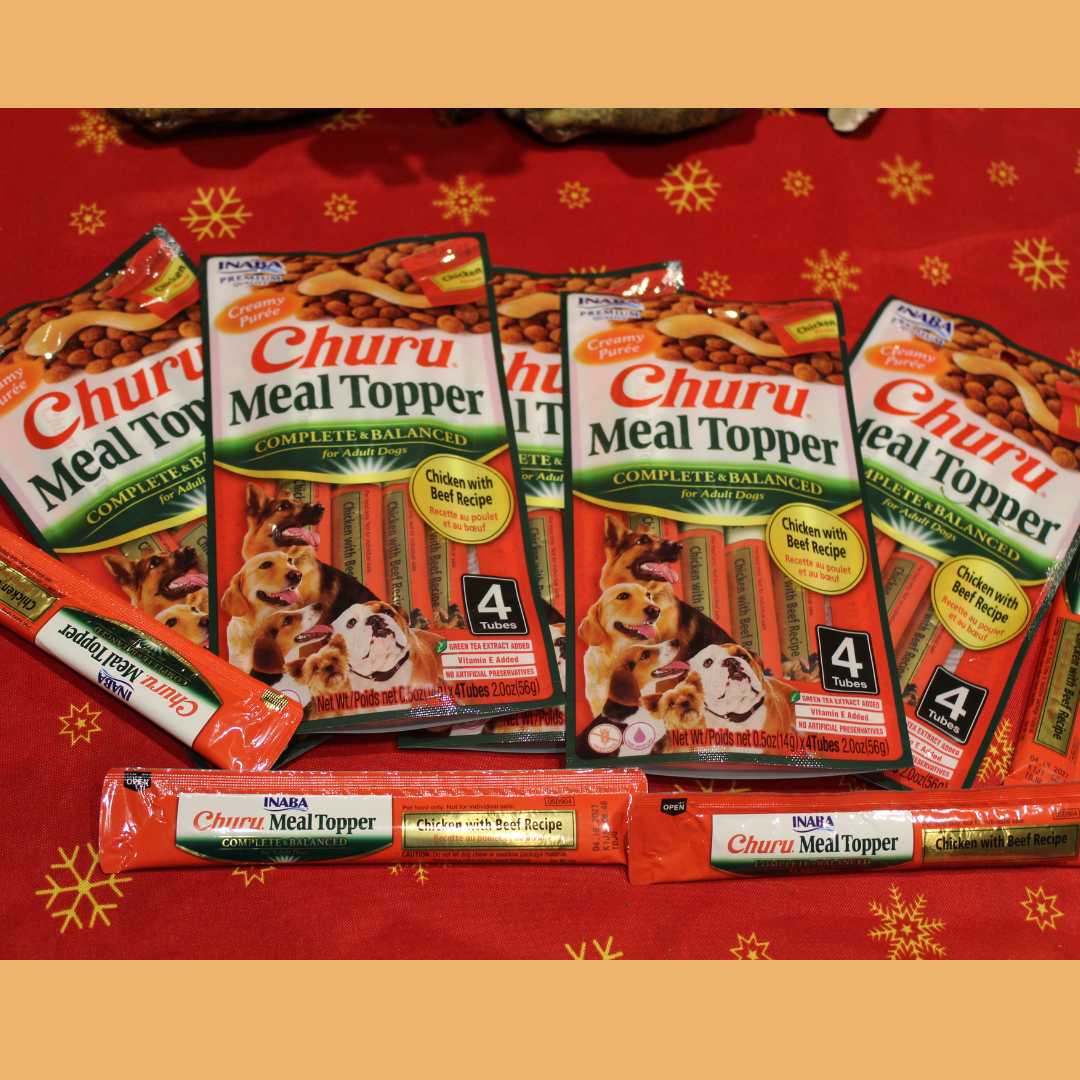 Fotografía de producto que muestra el empaque principal junto a los cuatro tubos individuales de Churu Meal Topper sobre un fondo cálido. Permite apreciar el formato práctico del snack listo para servir.