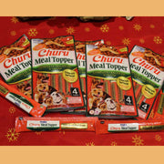 Fotografía de producto que muestra el empaque principal junto a los cuatro tubos individuales de Churu Meal Topper sobre un fondo cálido. Permite apreciar el formato práctico del snack listo para servir.